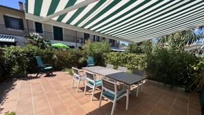 Un patio con una mesa y sillas, rodeado de plantas en macetas y un toldo a rayas.