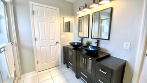 A bathroom with a white door, black vanity with two sinks, and three wall-mounted lights. - NEW!  Mai Casa- 3-Bdrm House w/ Private Pool, Near Beaches & IMG Academy (Bradenton)