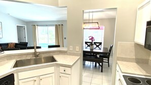 A modern kitchen with a built-in island, a dining area with a table and chairs, and a view of the living room. - NEW!  Mai Casa- 3-Bdrm House w/ Private Pool, Near Beaches & IMG Academy (Bradenton)