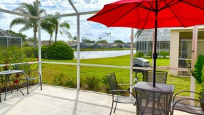 A covered patio with metal chairs and a table, overlooking a grassy area and a body of water. - NEW!  Mai Casa- 3-Bdrm House w/ Private Pool, Near Beaches & IMG Academy (Bradenton)