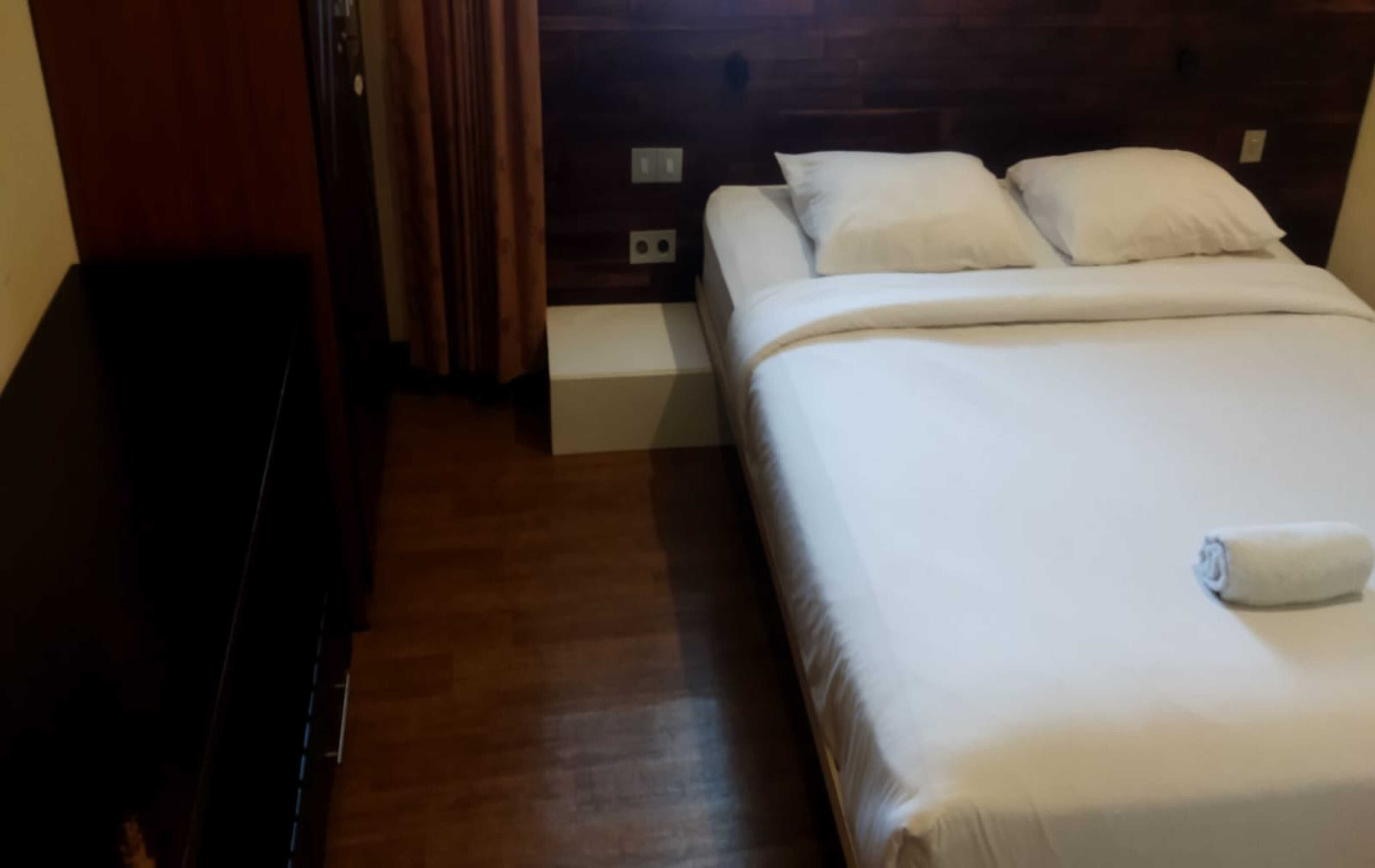 A hotel room with a wooden floor, a bed with white bedding, and a small bedside table.