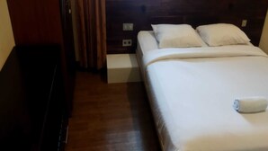 A hotel room with a wooden floor, a bed with white bedding, and a small bedside table. - Griya Joglo Kaliurang (Ngaglik)