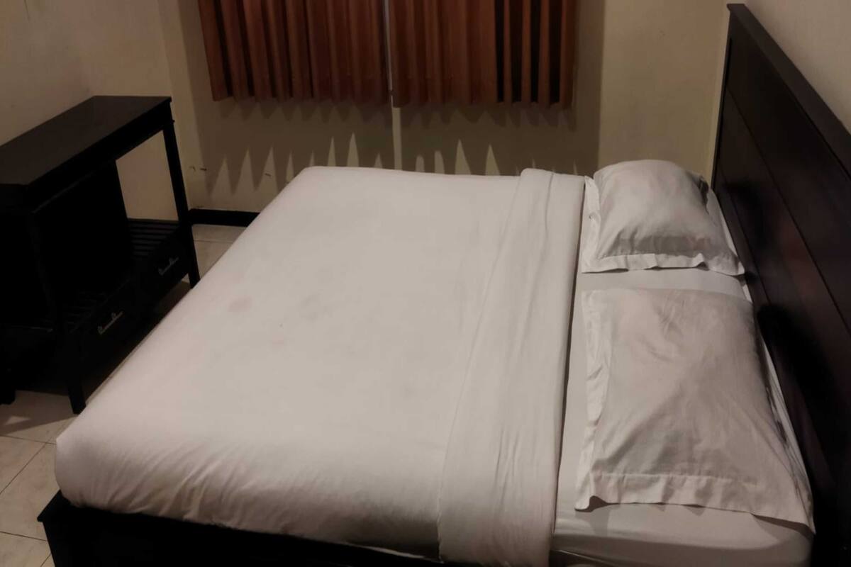 Una cama bien hecha con sábanas blancas en una habitación con un cabecero oscuro y una mesita de noche negra.