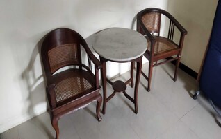 Una habitación pequeña con una mesa redonda y dos sillas de madera con asientos de mimbre.