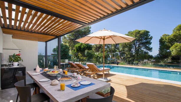 A modern outdoor dining area with a pool, wooden deck, and lounge chairs.