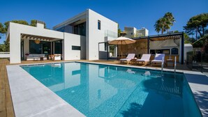 A modern pool area with a clear pool, lounge chairs, and a covered seating area.
