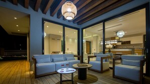 An outdoor seating area with a wooden deck, a sofa, two armchairs, a coffee table, and a chandelier.