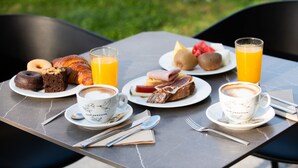 A breakfast table with croissants, pastries, fruit, and coffee cups. - Leonardo Hotel San Sebastián (San Sebastián)