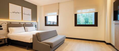 Ein modernes Hotelzimmer mit einem Bett, einer Couch, einem Fernseher und Kunstwerken an der Wand.