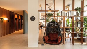 A modern interior with a hanging chair, wooden paneling, and a plant-filled shelving unit. - Leonardo Hotel San Sebastián (San Sebastián)
