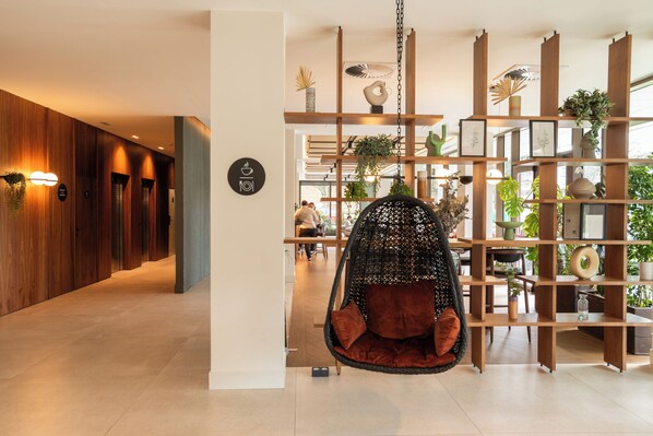 Un interior moderno con una silla colgante, paneles de madera y una estantería llena de plantas.