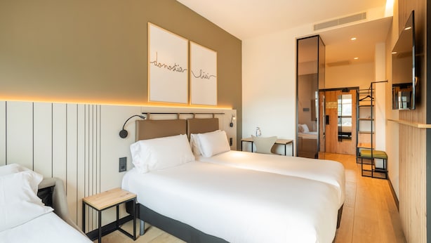 Ett modernt hotellrum med två sängar, ett litet bord och en spegel.