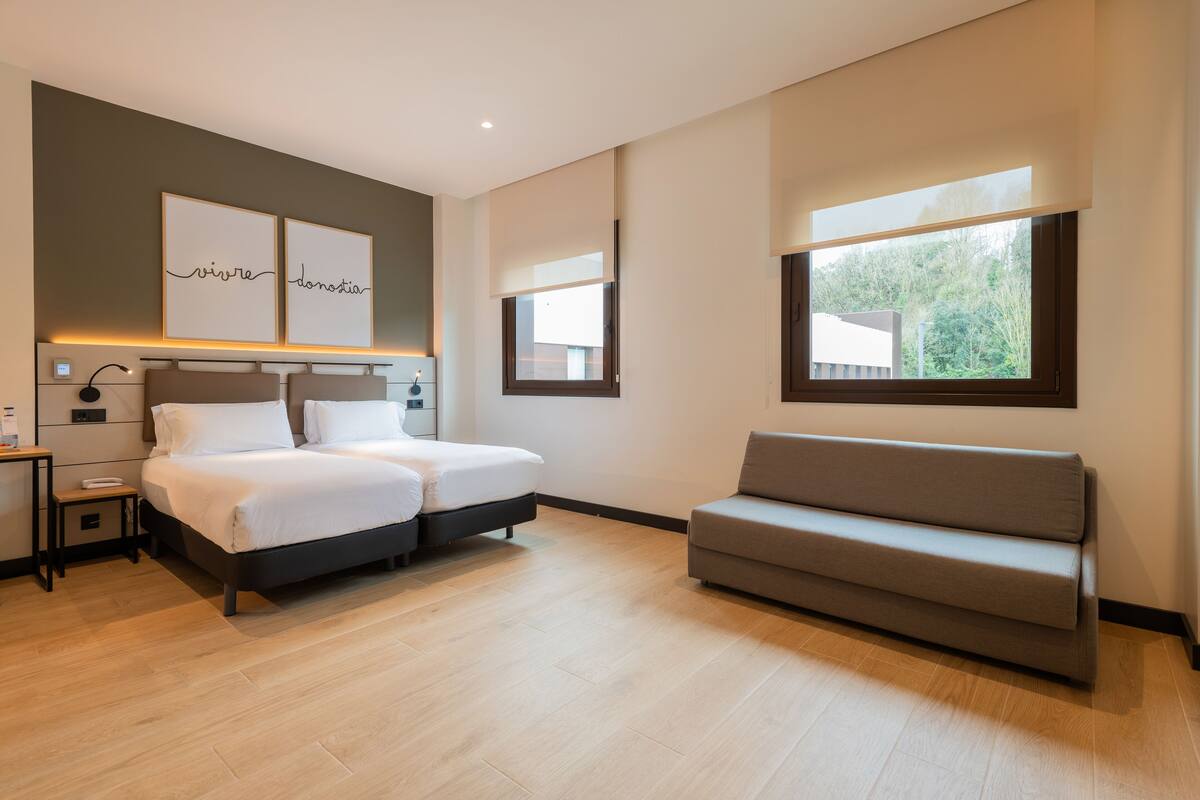 A modern bedroom with a double bed, bedside tables, a sofa, and artwork on the wall.