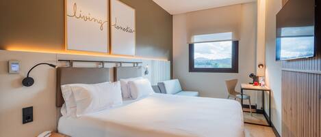 A modern hotel room with a large bed, a desk, a chair, and a TV.