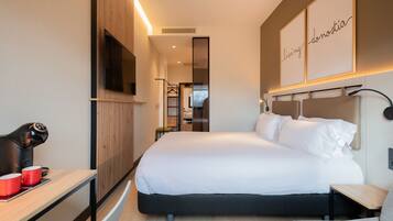 Una habitación de hotel moderna con una cama grande, un escritorio con cafetera y un espejo.