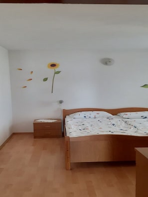 A bedroom with a wooden bed, a nightstand, and a wall decoration of a sunflower. - Apartments Biserka (Rab)