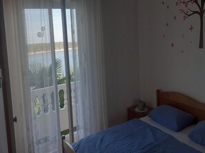 A bedroom with a bed, a nightstand, and a view of a balcony with a railing.