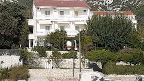 A multi-story building with balconies, surrounded by greenery and mountains.