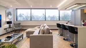 Een moderne woonkamer met een bank, een salontafel en een televisie. Er is een groot raam met uitzicht op gebouwen.