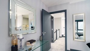 Een moderne badkamer met een glazen wastafelmeubel, een grote spiegel en een deur naar een slaapkamer.