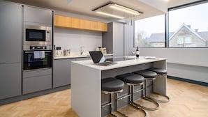 A modern kitchen with a central island, bar stools, and a large window. - Exquisite 2 Bed Duplex Apt | Secure Parking | (Penarth)