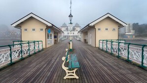 A wooden boardwalk with two buildings, a bench, and a 'NO FISHING' sign. - Exquisite 2 Bed Duplex Apt | Secure Parking | (Penarth)