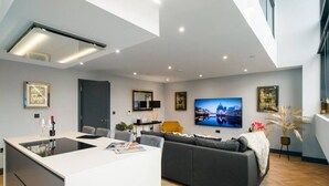 A modern living room with a central island, a sofa, a TV, and a dining area. - Luxe 2 Bed Duplex Apt w/Balcony, 3 Bathrooms, Free Parking (Penarth)