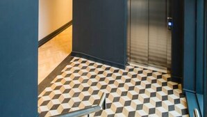 A modern elevator with a metallic finish, a checkered floor pattern, and a hanging light fixture with spherical bulbs. - Luxe 2 Bed Duplex Apt w/Balcony, 3 Bathrooms, Free Parking (Penarth)