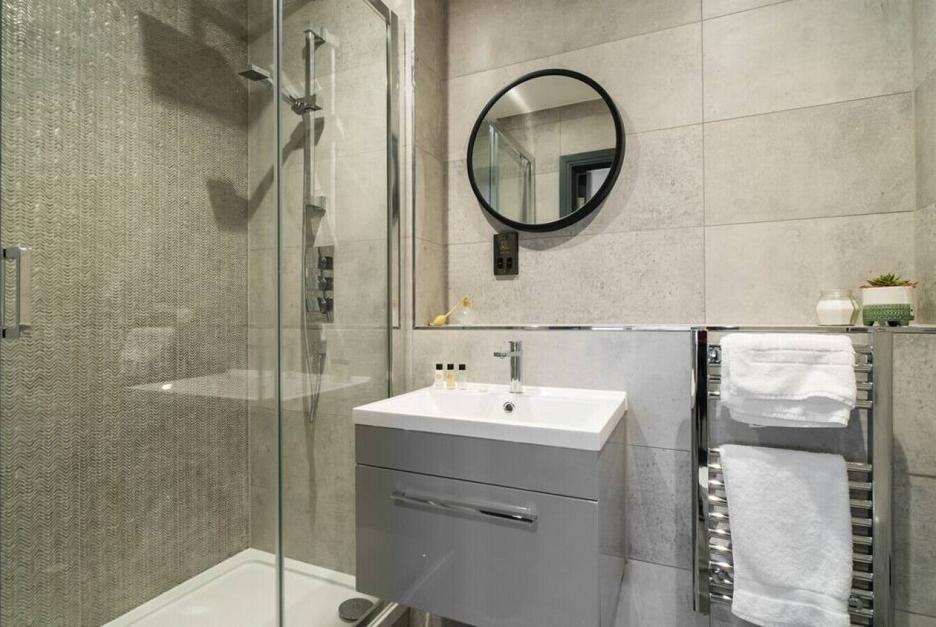 Un baño moderno con cabina de ducha de vidrio, un lavamanos blanco y un espejo.