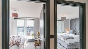 Moderni hotellihuone, jossa on suuri sänky, työpöytä, jossa on maapallo, ja suuret ikkunat, joista avautuu näkymä kaupunkiin.