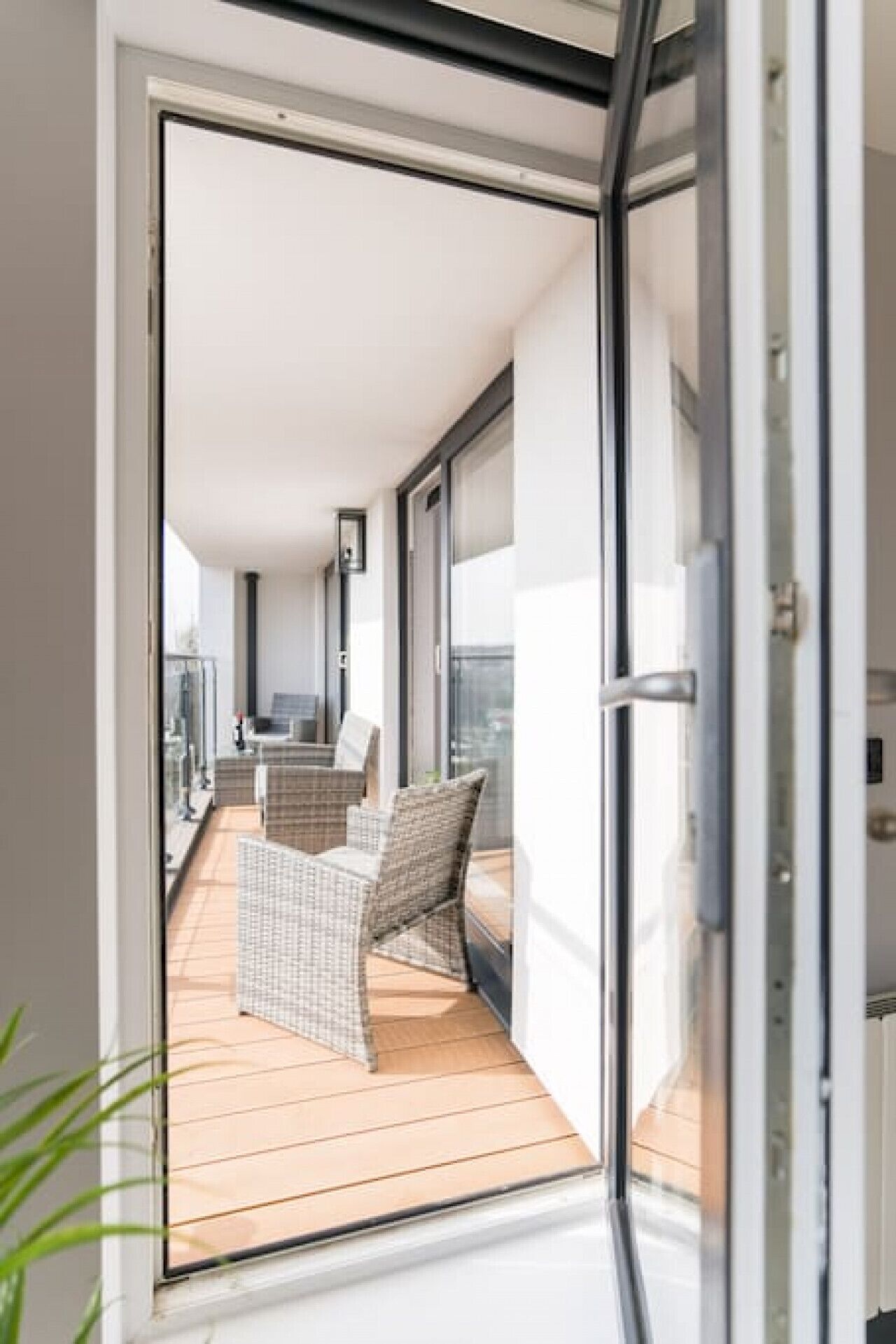 A modern balcony with wicker furniture and a glass door leading to a room.