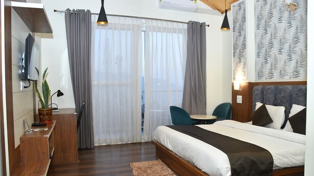 A modern hotel room with a wooden bed, a desk, a chair, and a TV. - Hotel Le Halcyon (Solan)