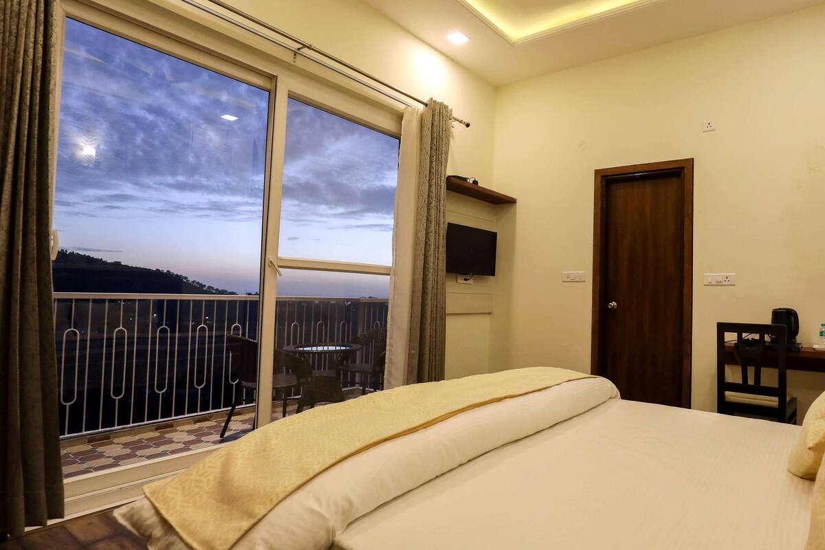 A hotel room with a large bed, a desk with a chair, a TV, and a view of the outdoors.