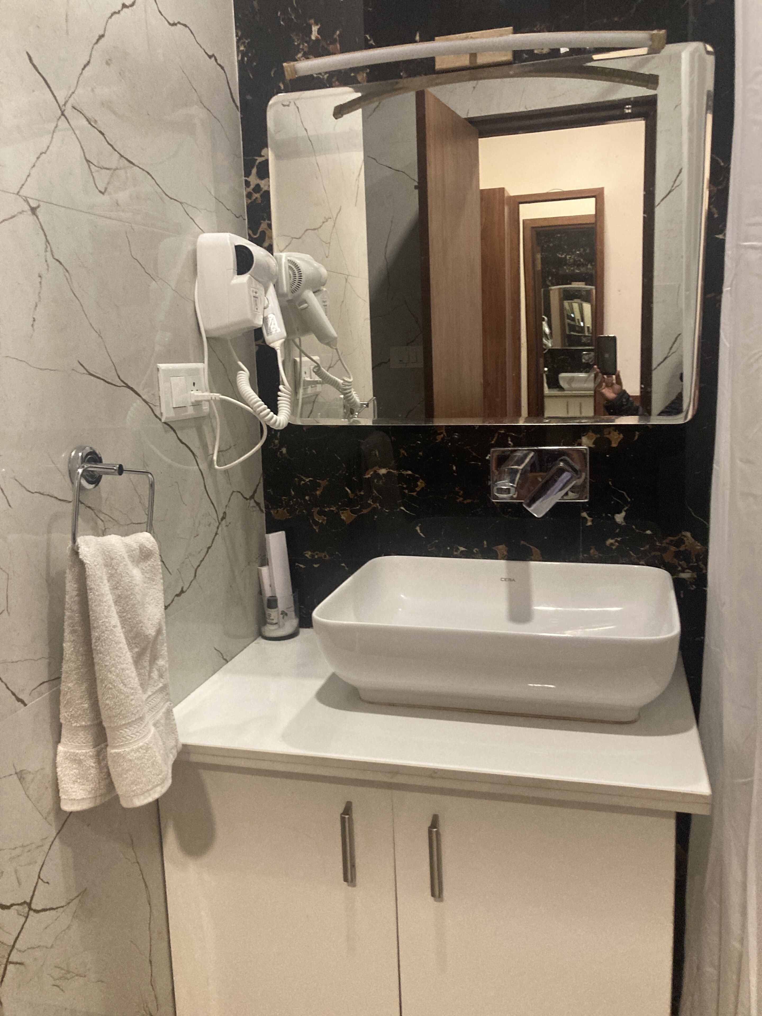 Un bagno con lavandino bianco, porta asciugamani, asciugacapelli e specchio.