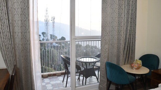 A balcony with a table and chairs, a bag of snacks, and a view of a mountain and communication tower. - Hotel Le Halcyon (Solan)