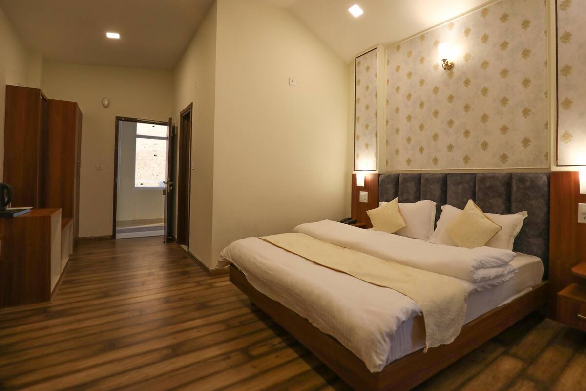 A hotel room with a large bed, wooden flooring, a desk, and a wardrobe.