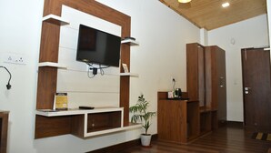A modern living room with a flat-screen TV mounted on a wooden wall unit, a potted plant, and built-in wooden cabinets. - Hotel Le Halcyon (Solan)