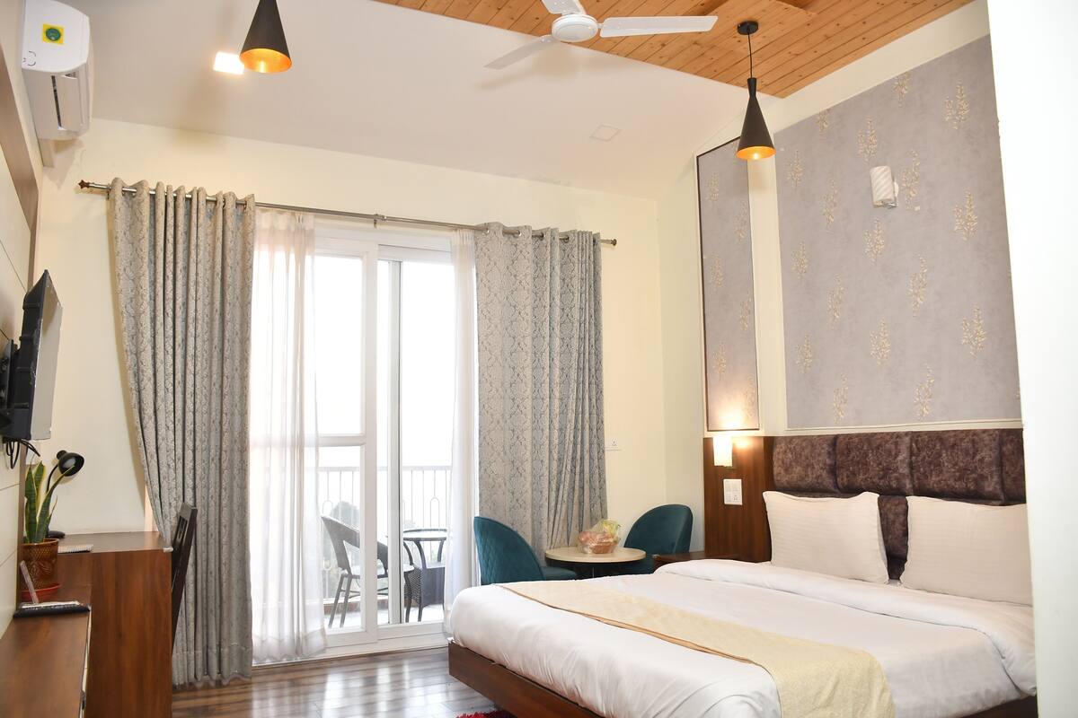 A hotel room with a bed, a desk, a chair, a table, and a balcony with a chair.