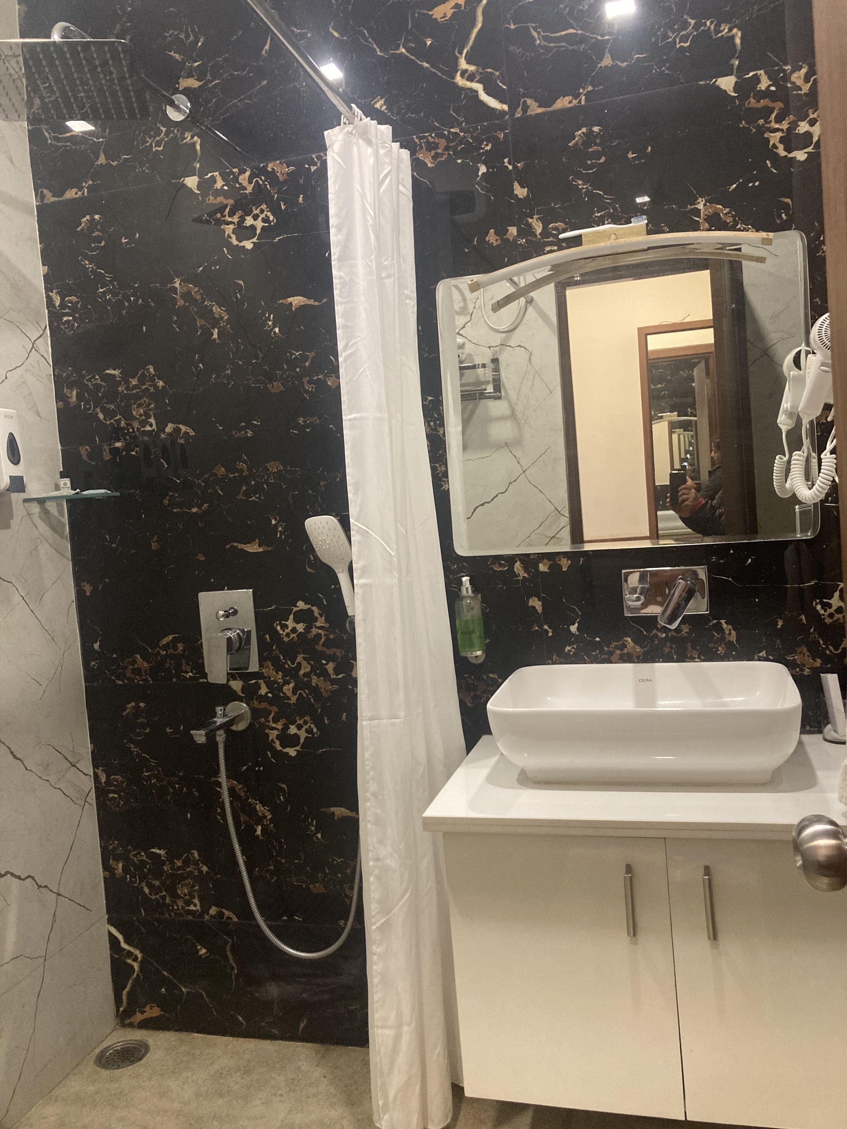 A bathroom with a black marble wall, a white sink, and a shower area.