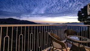 A balcony with wicker chairs and a glass table, overlooking a mountainous landscape at dusk. - Hotel Le Halcyon (Solan)