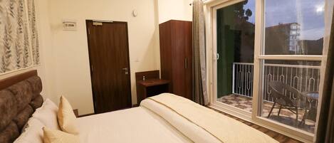 A hotel room with a bed, a wardrobe, a small table, and a balcony with a chair.
