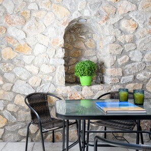 A stone wall with a green potted plant, a wicker chair, a table with a book and two glasses of green drink.
