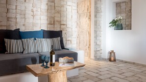 Un salon moderne avec un canapé gris, des coussins à rayures, une table basse en bois sur laquelle reposent des verres à vin et une bouteille, et un mur dont le motif rappelle celui d'un mur en briques.