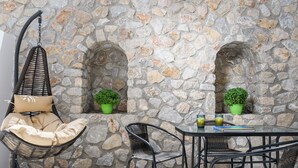Un mur de pierre avec deux arcades, une chaise suspendue et une table avec des chaises.