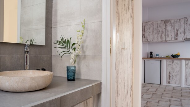 Une salle de bain avec un lavabo en marbre, un miroir et un vase contenant des fleurs blanches.