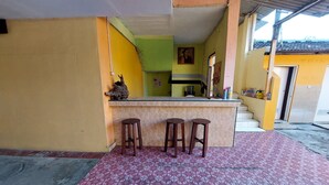 Un petit espace bar avec un comptoir et trois tabourets, un sol carrelé et un escalier menant à un niveau supérieur.