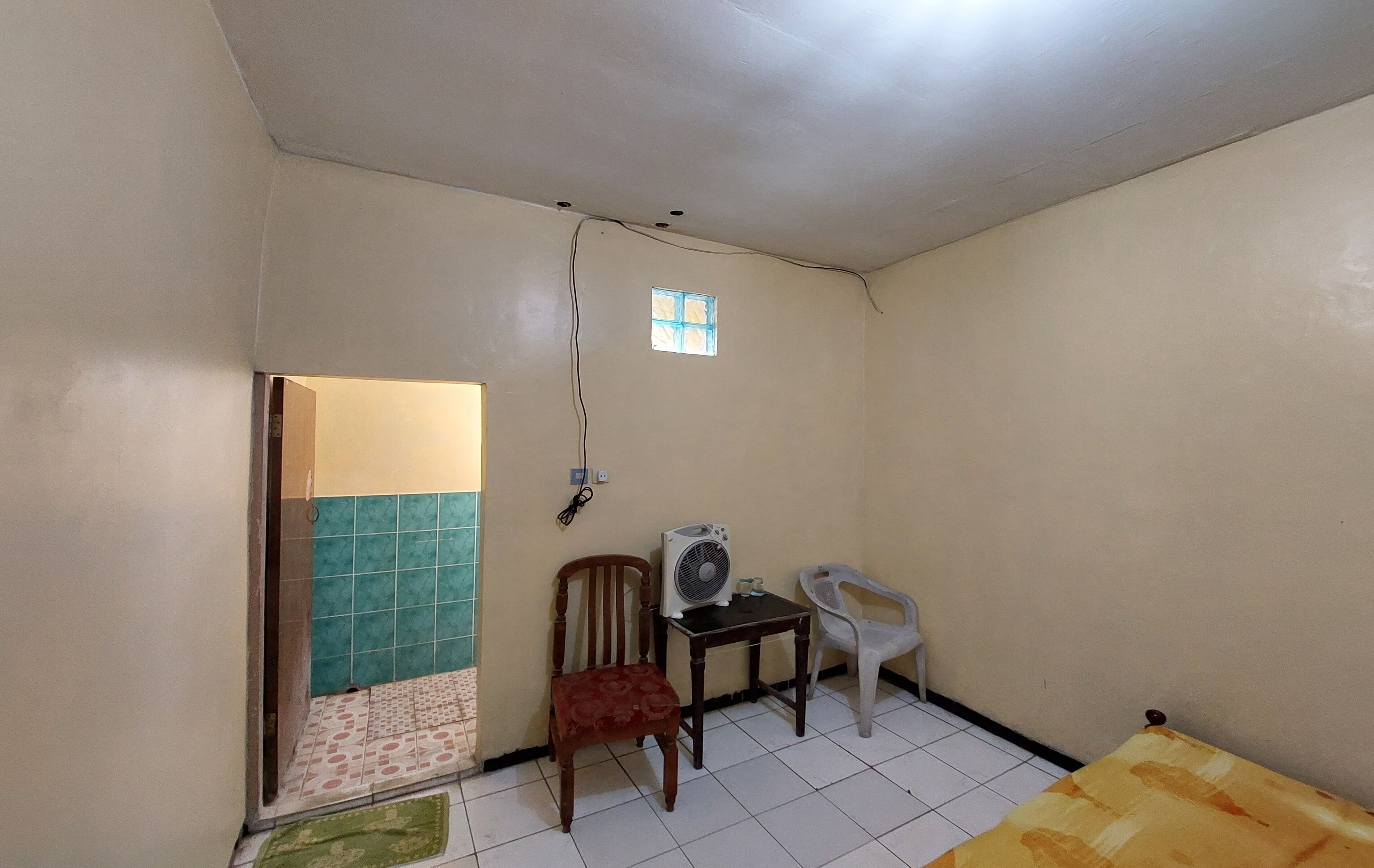 A small room with a tiled floor, a wooden chair, a plastic chair, a table, a window, and a door.