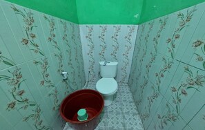 A small bathroom with floral patterned tiles, a white toilet, and a red bucket.