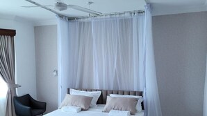 A modern bedroom with a large bed, a ceiling fan, and sheer curtains.