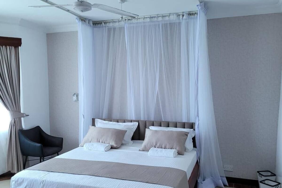 A modern bedroom with a large bed, a ceiling fan, and sheer curtains.